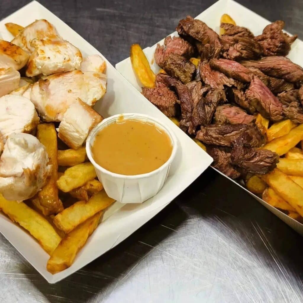 Deux barquettes de plats à emporter : poulet grillé et frites avec sauce d'un côté, et steak coupé en lanières et frites de l'autre.